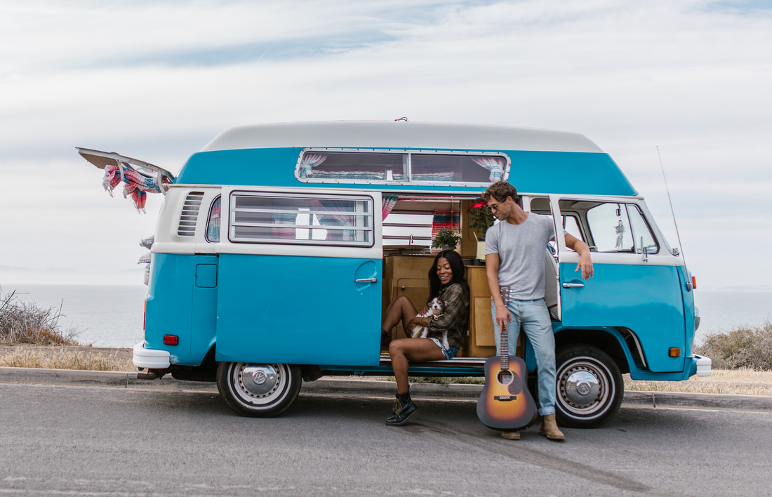 A couple with a guitar and a puppy sitting in their van on a road trip.